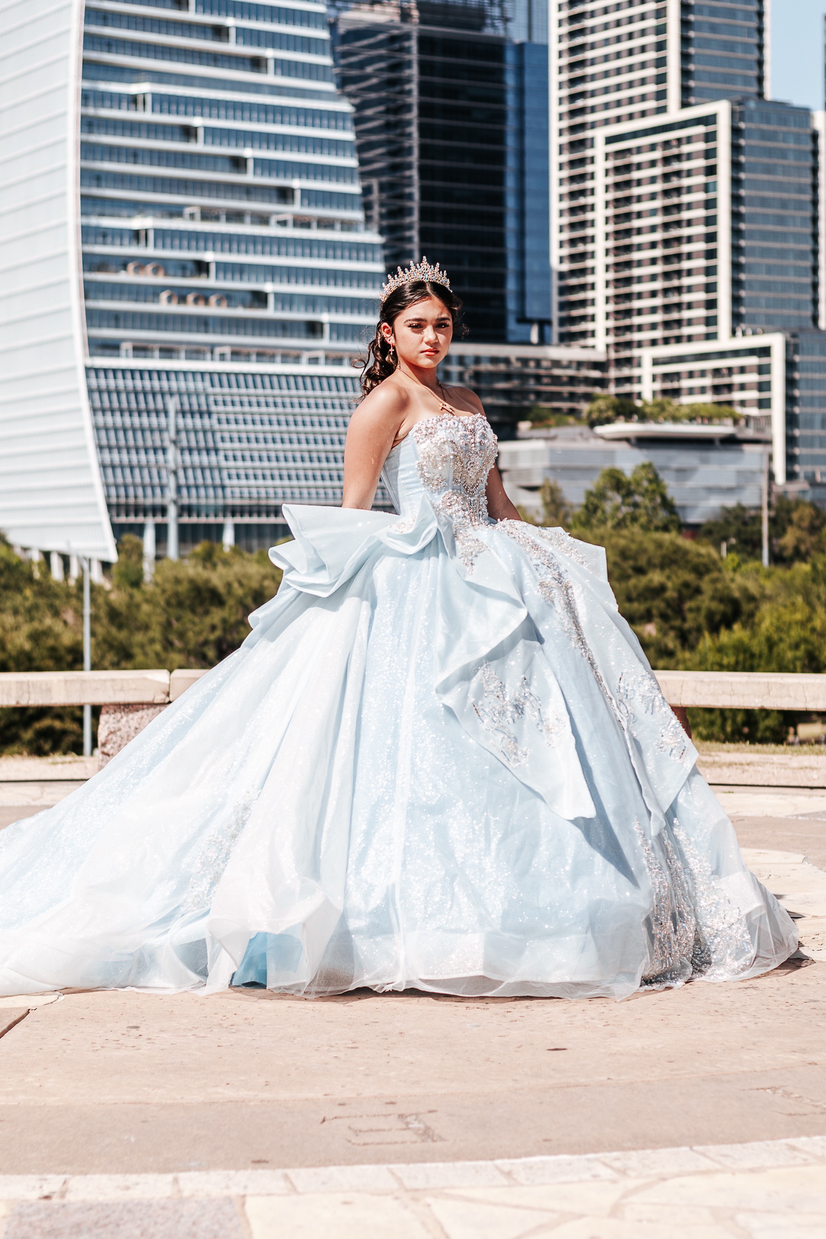 Quinceañera in a light blue ball gown and tiara posing in front of the downtown Austin skyline, photographed by Weddings by Wendi