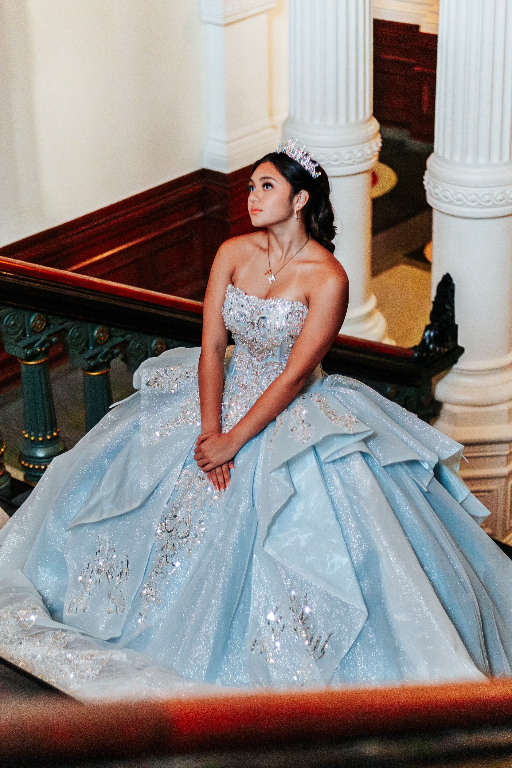 Quinceañera seated on the Texas State Capitol staircase looking upward, tiara catching the light, photographed by Weddings by Wendi