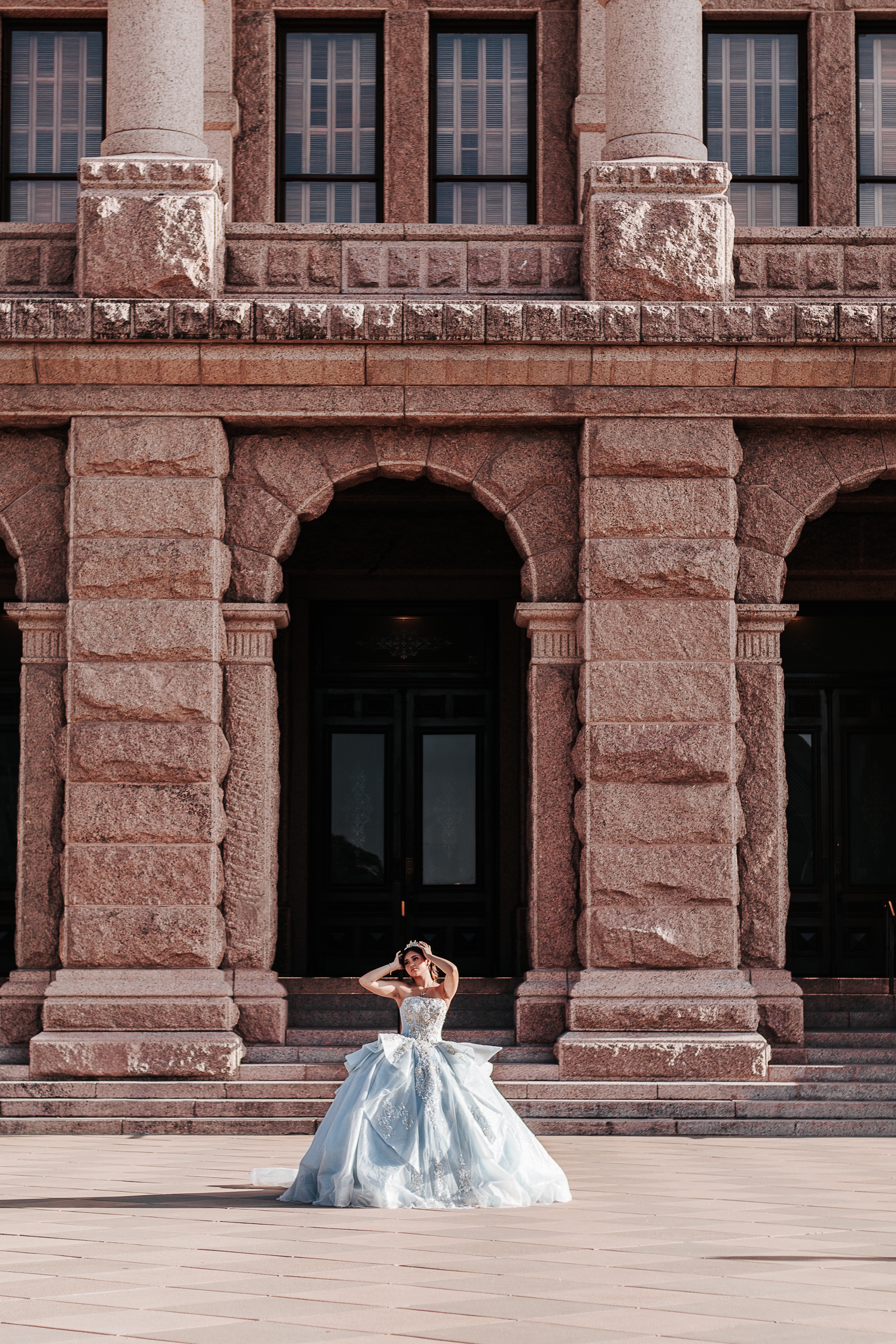 Quinceañera adjusting her tiara in front of the Texas State Capitol facade in Austin, photographed by Weddings by Wendi