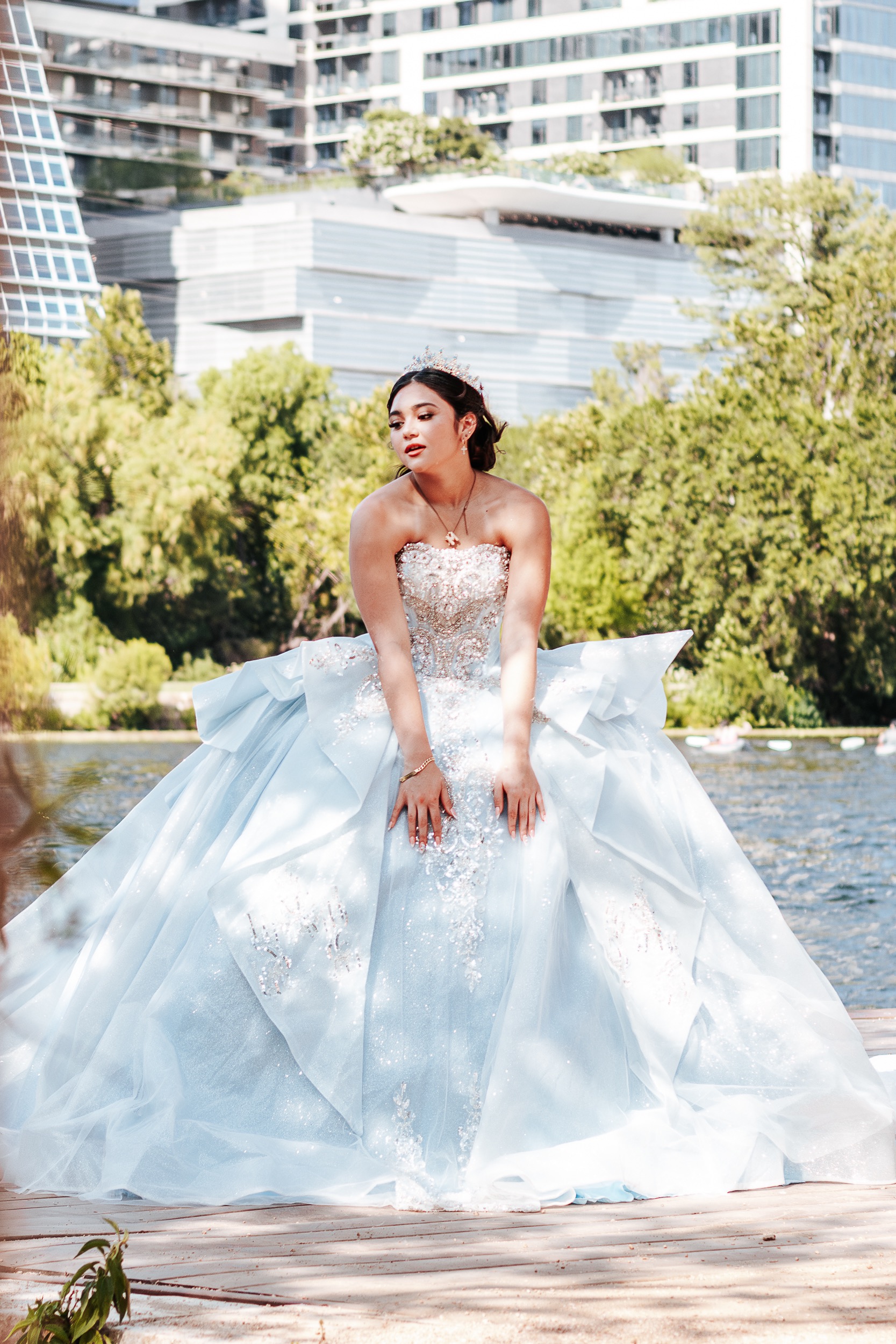 Quinceañera leaning forward on a dock over Lady Bird Lake with the Austin skyline in the background, photographed by Weddings by Wendi