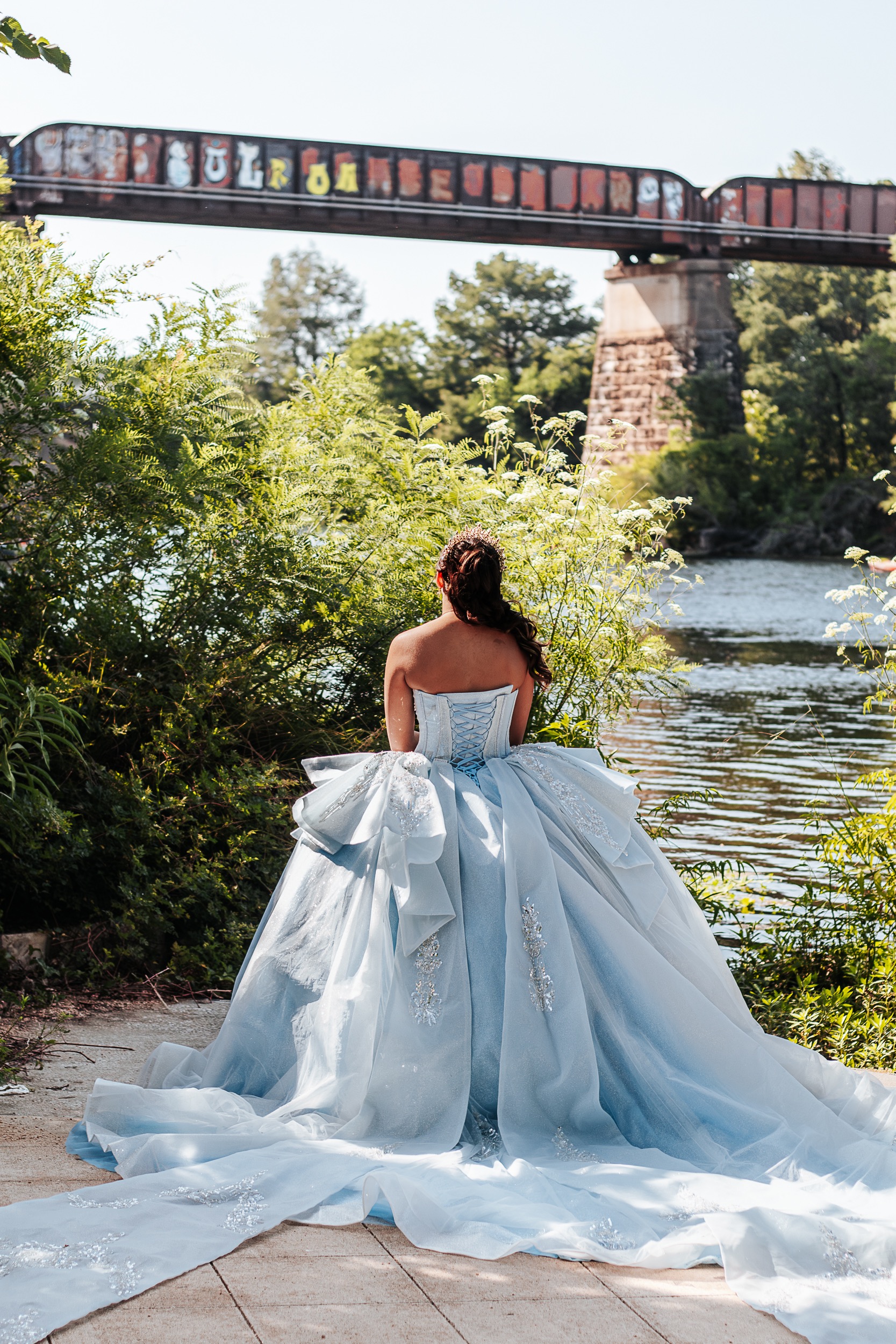 Quinceañera from behind facing a river with a historic railroad bridge overhead in Austin, photographed by Weddings by Wendi