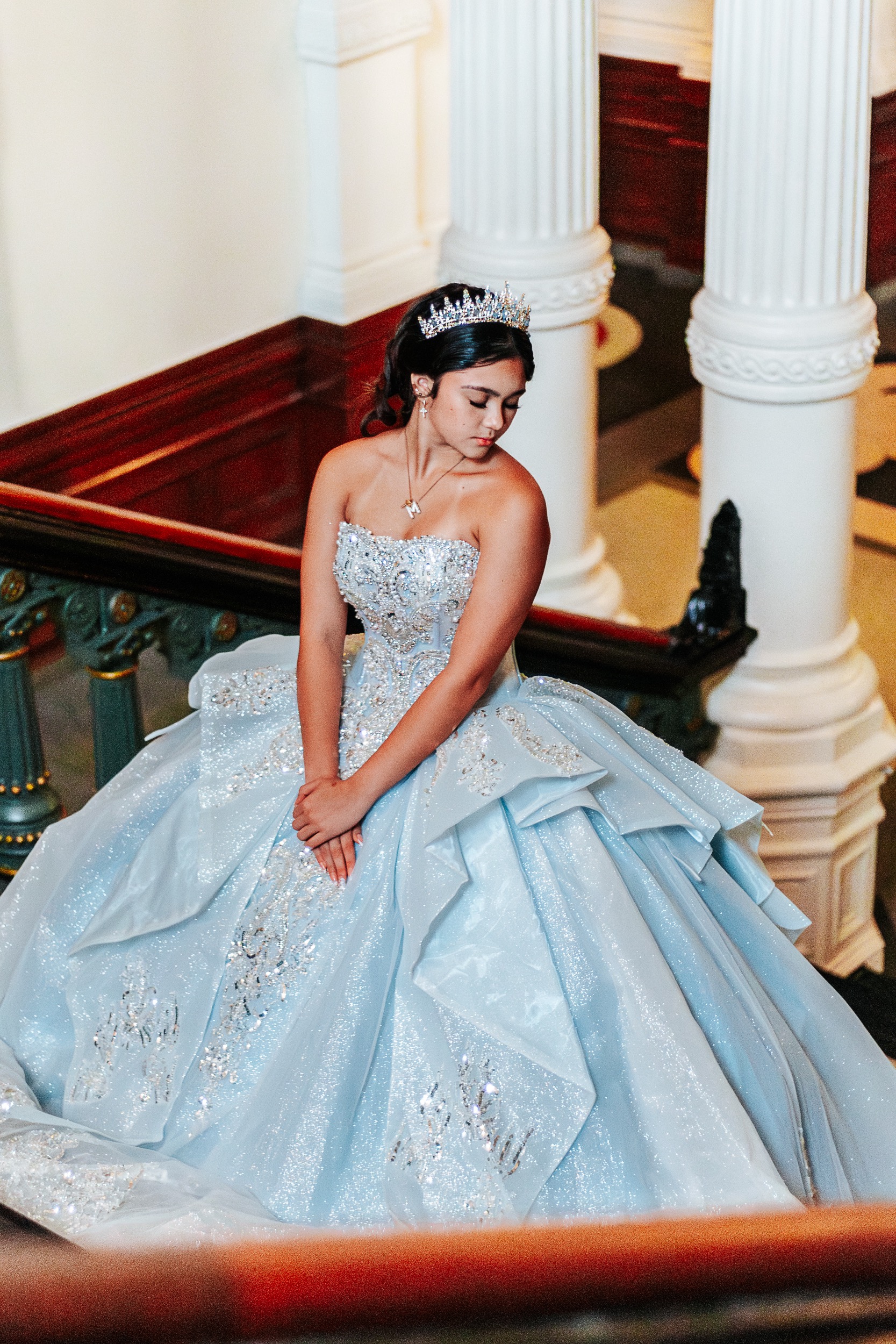 Quinceañera seated on the Texas State Capitol staircase looking down at her beaded gown, photographed by Weddings by Wendi