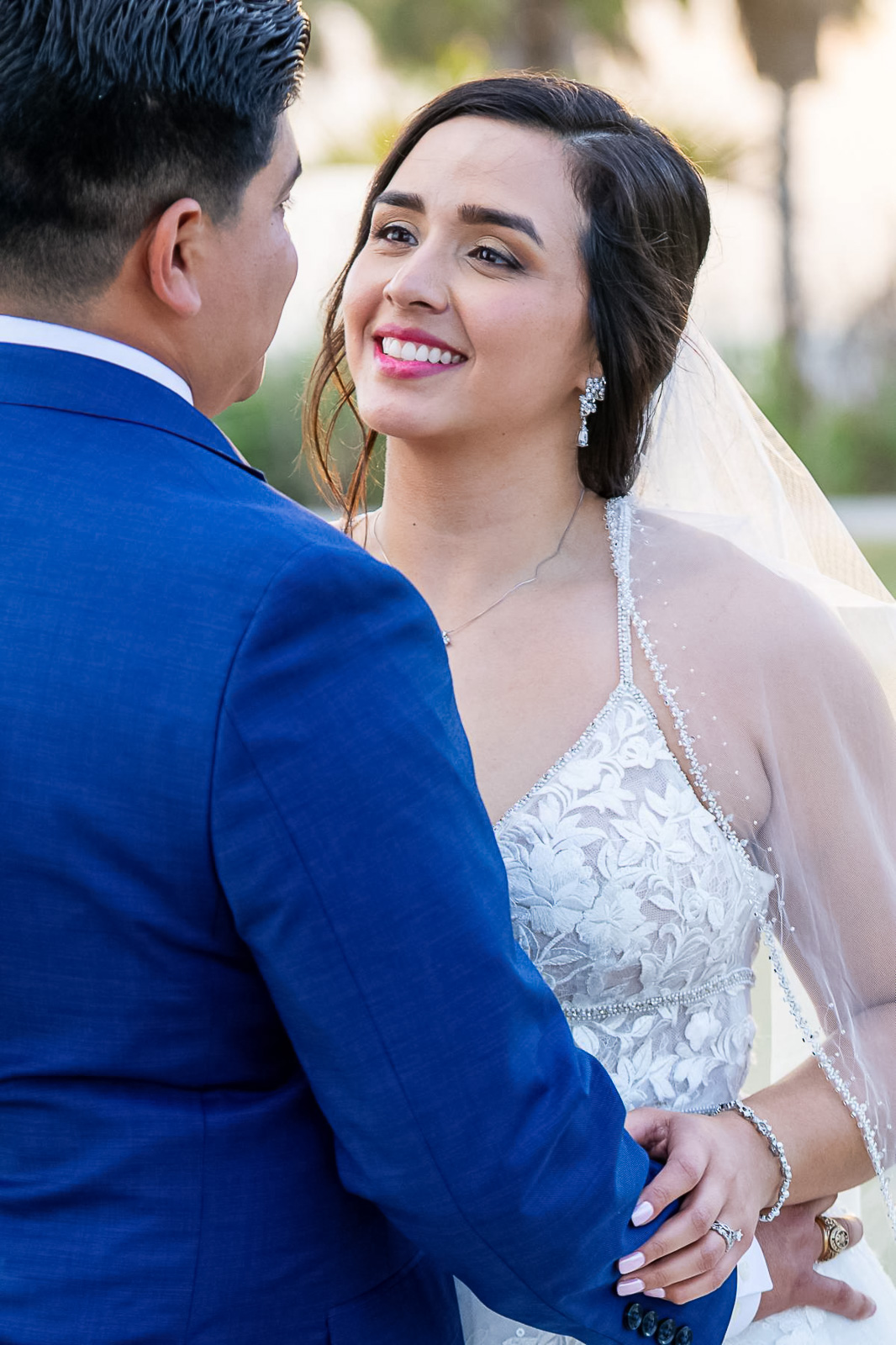 Bride smiling at groom during ceremony, bride in lace gown and groom in blue suit