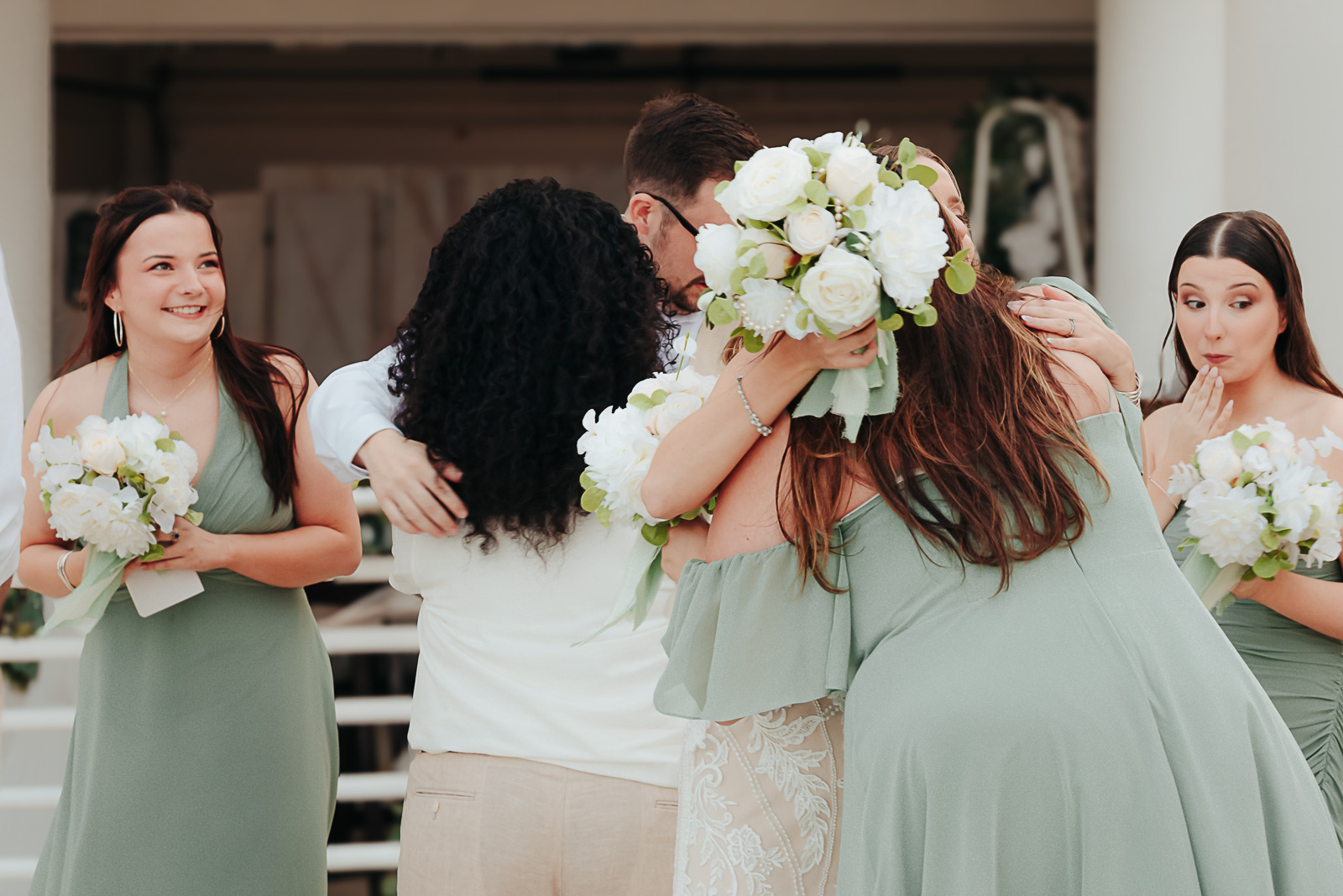 Bride and wedding party embracing in a group hug, bridesmaids in sage green gowns