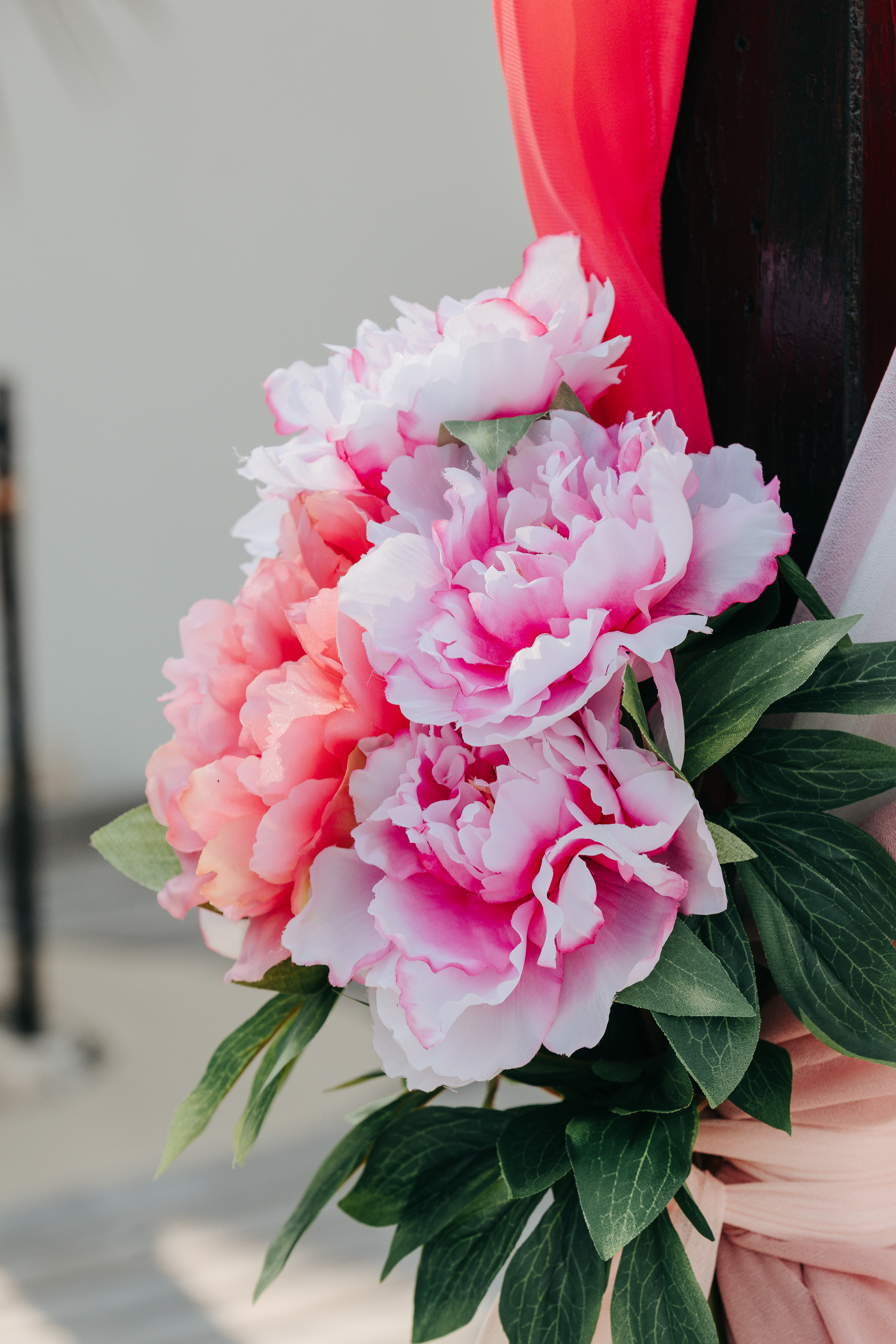 Wedding bouquet detail showing pink peonies and white flowers with green foliage tied with ribbon