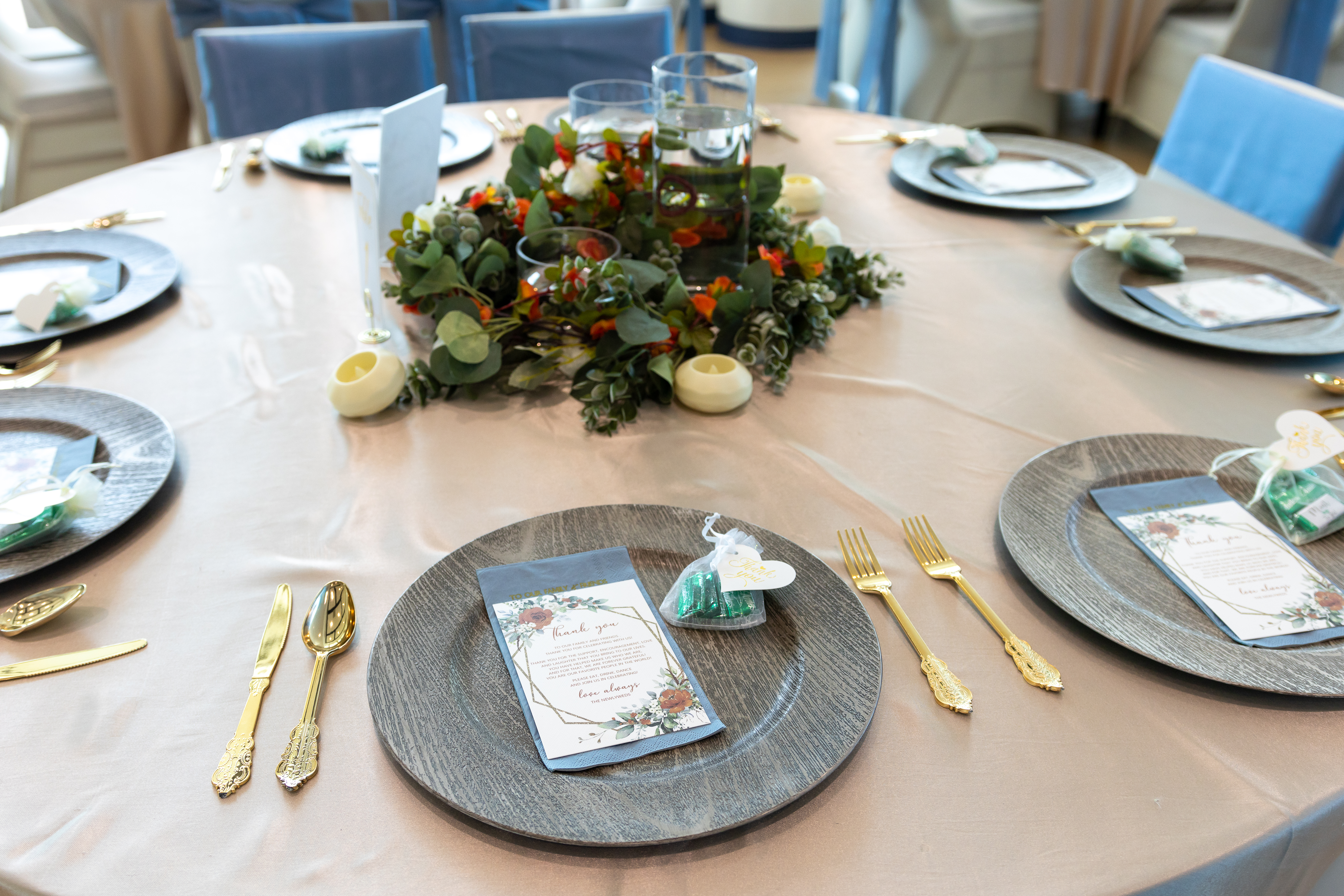 Reception table with stacked linens, gold flatware, and delicate centerpiece arrangement